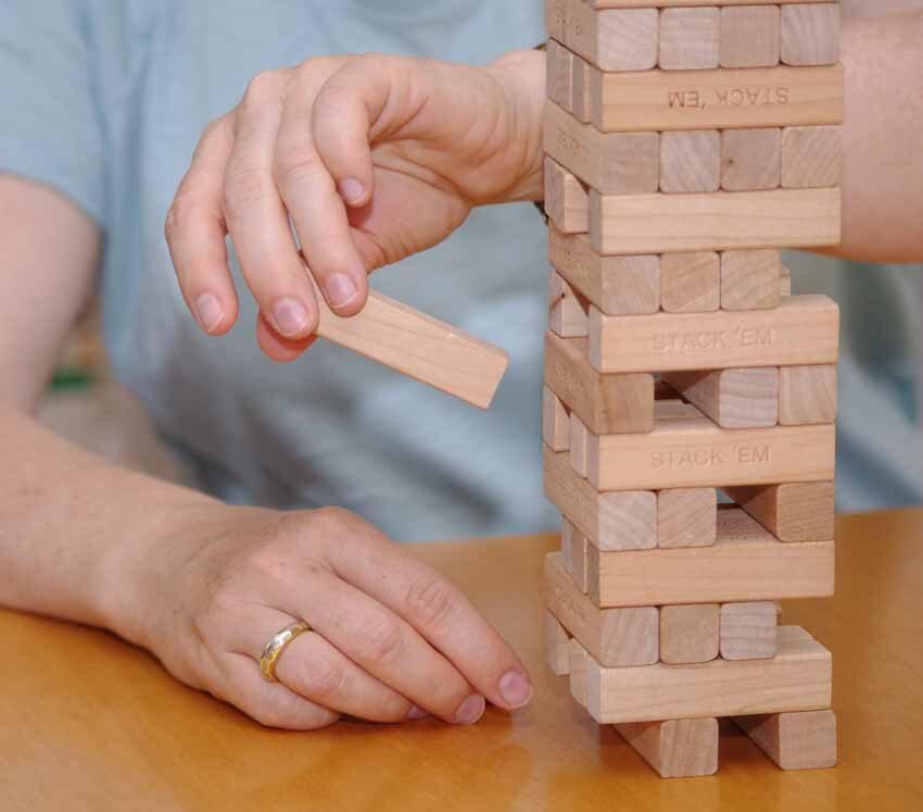 Hände ziehen einen Holzklotz aus einem Jenga-Turm auf einem Tisch