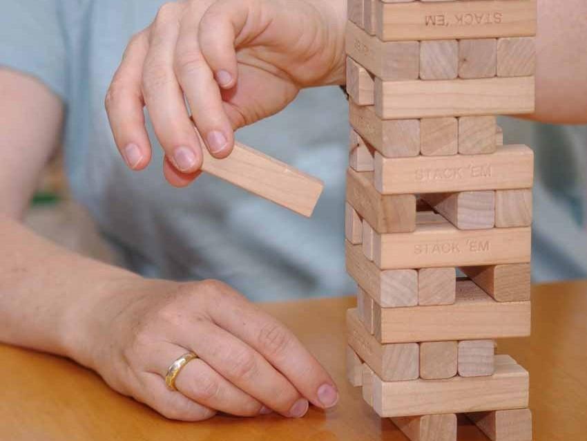Hände ziehen einen Holzklotz aus einem Jenga-Turm auf einem Tisch
